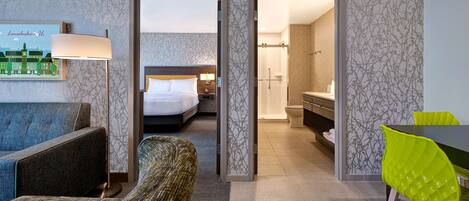 A hotel room with a bed, a desk, a chair, a lamp, and a bathroom visible through an open door.
