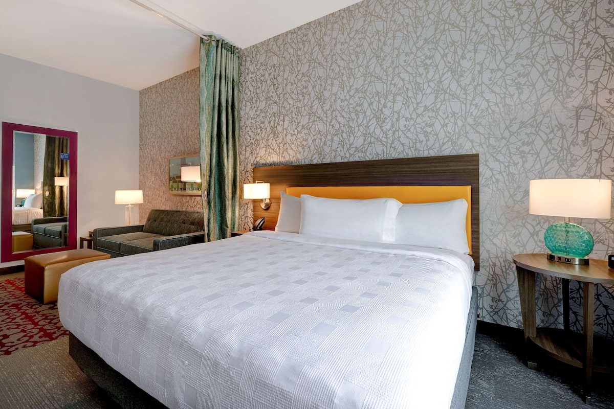 Una camera d'albergo con un letto grande, una zona relax con una poltrona e un tavolino, uno specchio e una parete decorata.