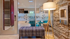A reception area with a glass door, a bench, a lamp, and a wall with a stone pattern. - Home2 Suites by Hilton Lincolnshire Chicago (Lincolnshire)