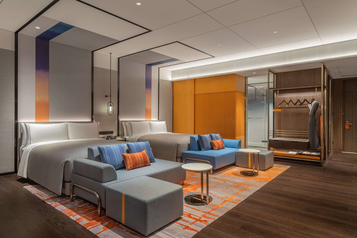 A modern hotel room with a large bed, two sofas, a small table, and a walk-in closet with a mirror and clothing rack.
