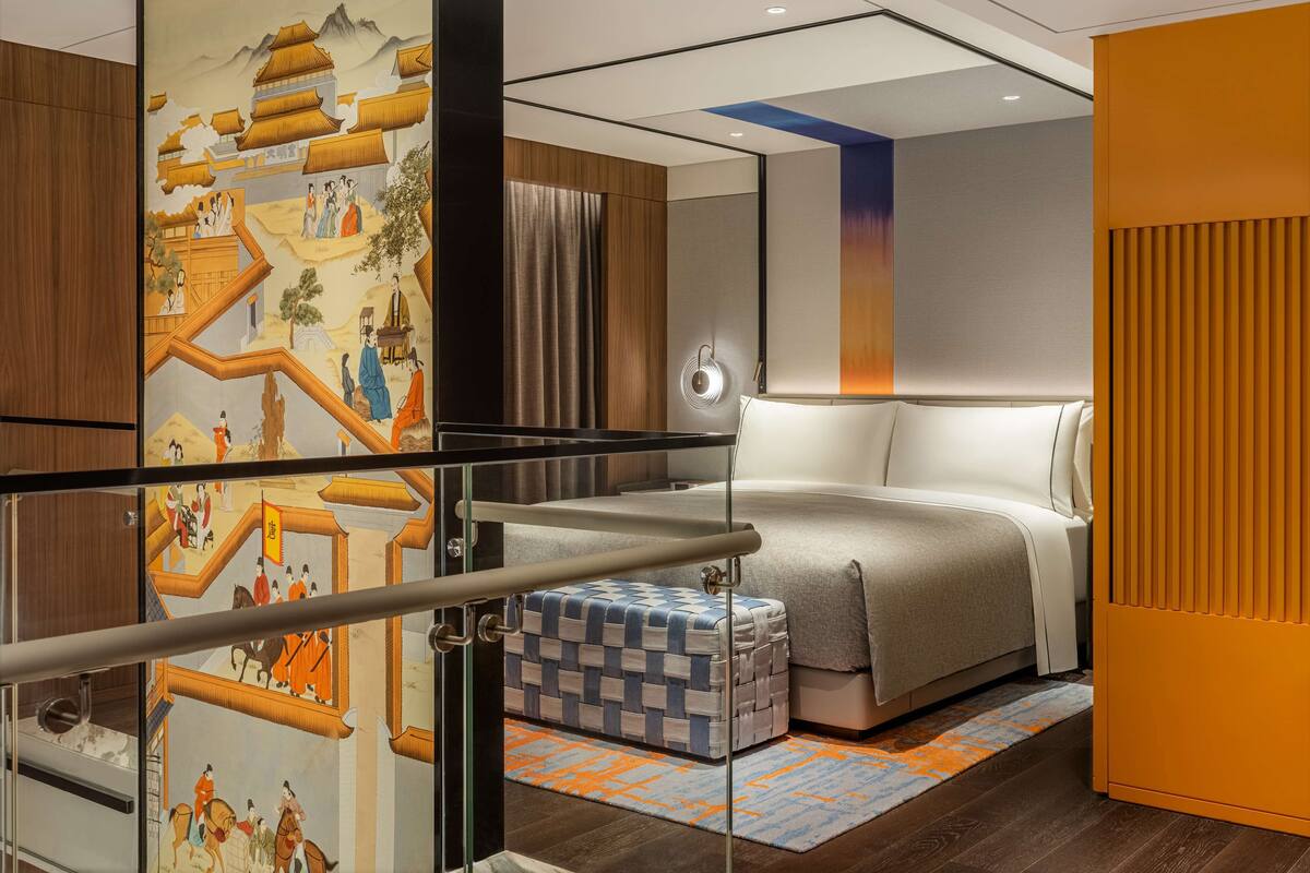A modern hotel room with a large bed, a small seating area, and a decorative wall with traditional artwork.