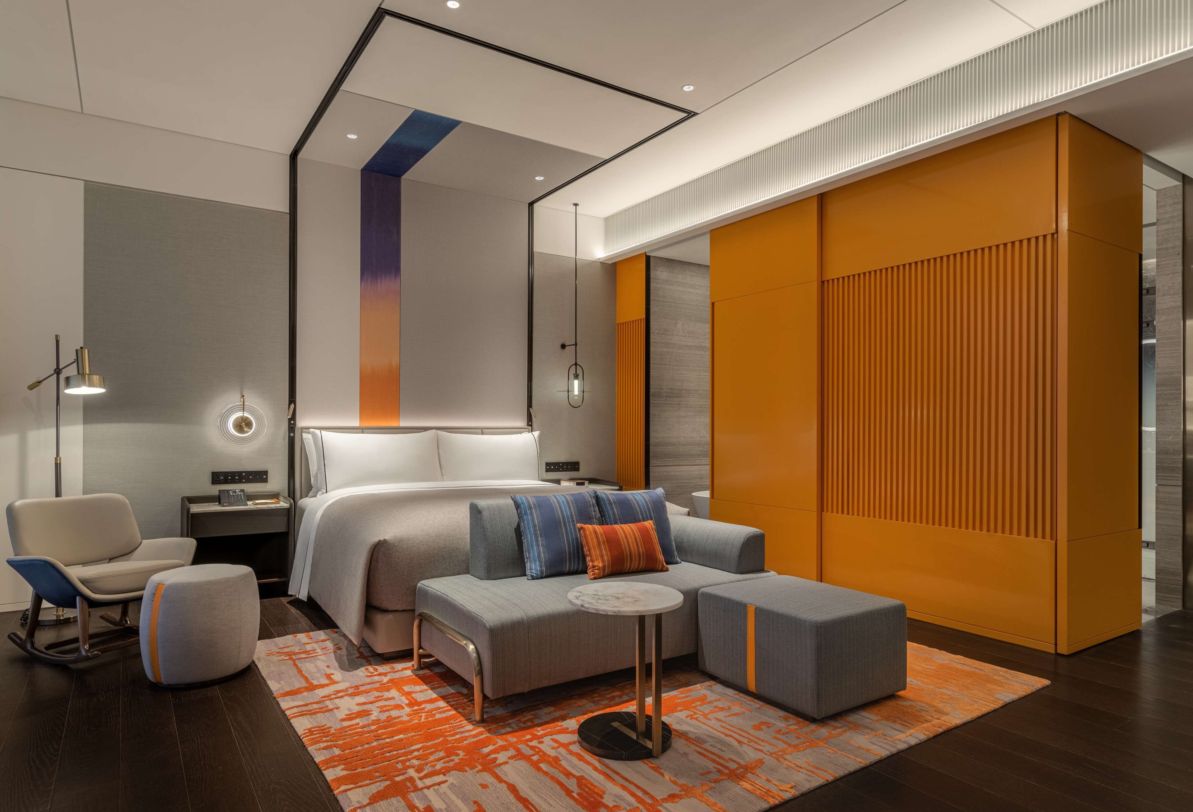 A modern hotel room with a large bed, a sofa, a small table, and a chair.