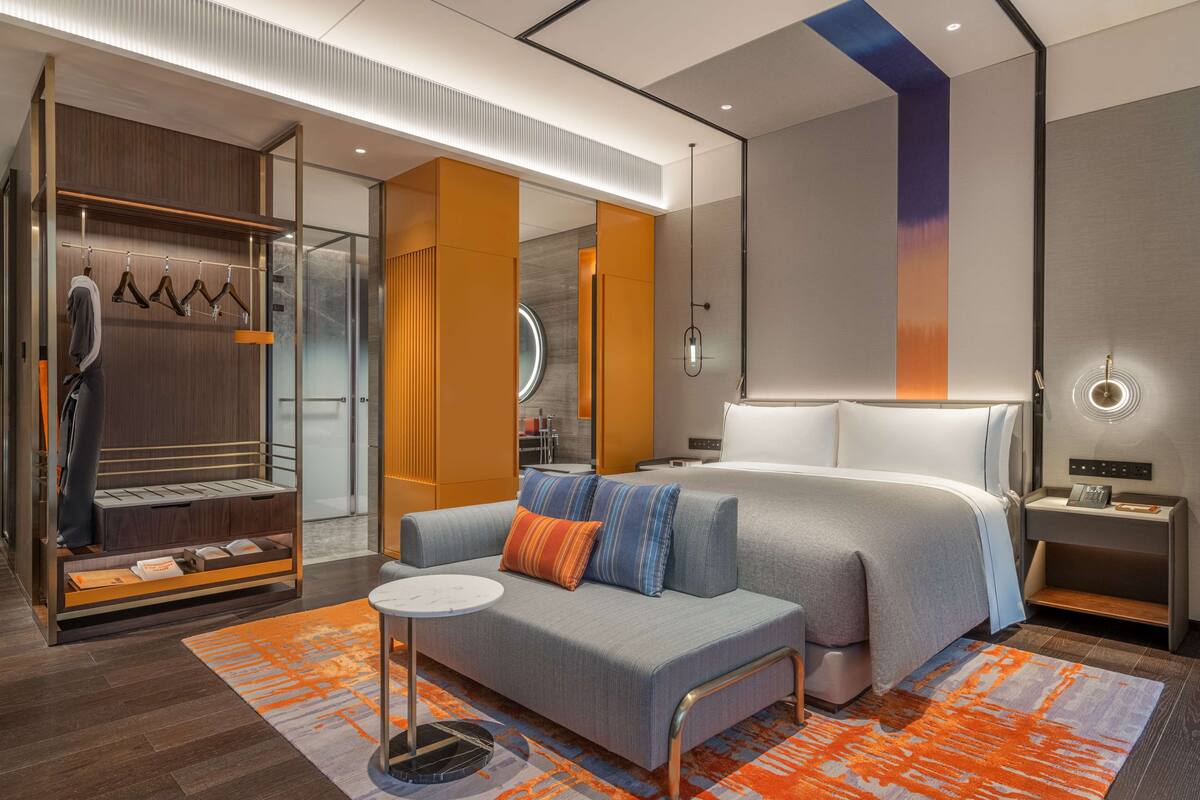 A modern hotel room with a large bed, a seating area, a wardrobe, and a bathroom visible through an open door.