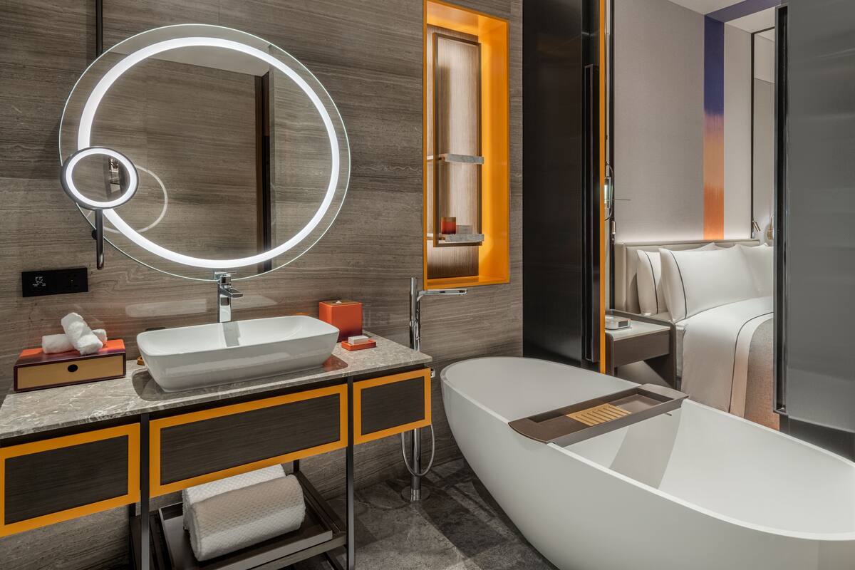 A modern bathroom with a freestanding bathtub, a large mirror with a circular light, and a wooden vanity.