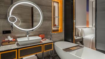 A modern bathroom with a freestanding bathtub, a large mirror with a circular light, and a wooden vanity.