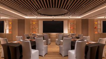 A conference room with a large screen, multiple tables, and chairs.