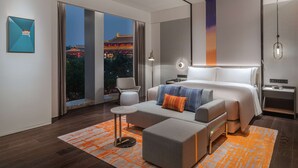 A modern hotel room with a large bed, a sofa, a small table, and a view of a traditional building at night. - Canopy by Hilton Xi'an Qujiang (Xi'an)