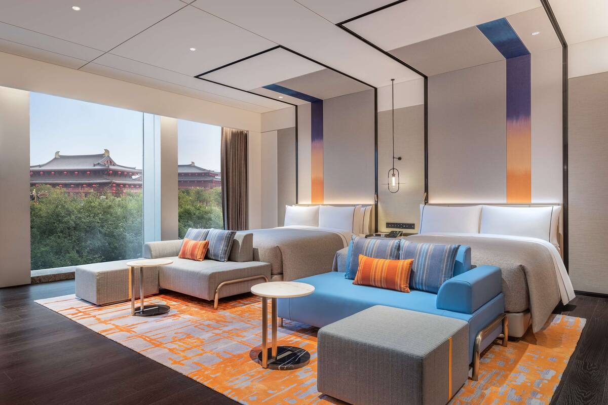 A modern hotel room with a large bed, a sofa, a small table, and a view of traditional architecture outside.
