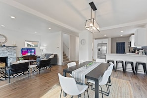 A modern kitchen with a central island, a dining area with a long table, and a living room with a fireplace.