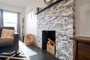 Uma sala de estar com lareira de pedra, um sofá, uma cesta de vime e uma caixa de madeira com a etiqueta 'DESIGNED BROOKLYN NEW YORK'.