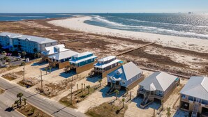 A coastal hotel with multiple buildings, a beach in the background, and a clear sky. - Blue Pearl | great august rates. Pool. Hottub. On Beach (Dauphin Island)