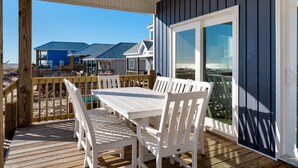 A covered outdoor area with a wooden deck, white furniture, and a view of beach houses. - Blue Pearl | great august rates. Pool. Hottub. On Beach (Dauphin Island)