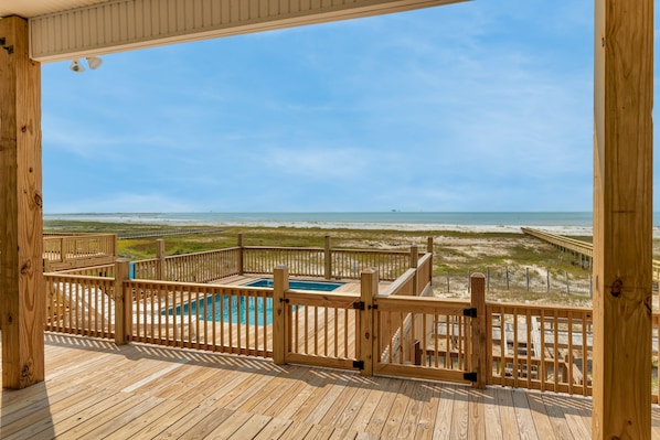 A wooden deck with a pool and a beach view.