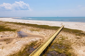 A long yellow bridge over a beach with sand dunes and a clear sky.