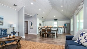 A spacious living room with a dark brown coffee table, a blue sofa with star-patterned pillows, and a large brown rug. - Sunny and 75 | August 1 opening. Pool, Gulf Front (Dauphin Island)