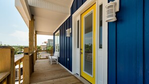 A wooden deck with a covered area, a yellow door, and a white wall with a window. - Sunny and 75 | August 1 opening. Pool, Gulf Front (Dauphin Island)