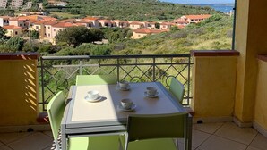 Un balcon avec une table et des chaises, donnant sur une colline parsemée de bâtiments et offrant une vue sur un ciel dégagé.