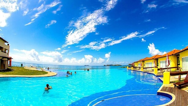 Una grande piscina esterna con vista sull'oceano, circondata da edifici con tetti rossi.