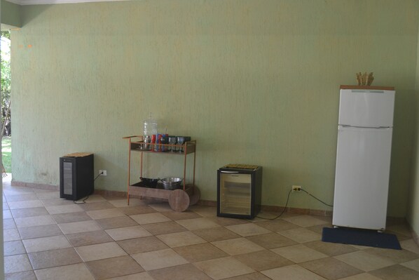 A kitchen with a refrigerator, a small refrigerator, a shelf with kitchen utensils, and a microwave.