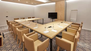 Un salón de conferencias con una larga mesa, varias sillas, un televisor y una pizarra.