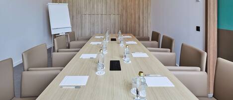 Ein Konferenzraum mit langem Tisch, Stühlen, einer Whiteboard und Wasserflaschen.