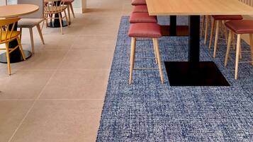 Un comedor moderno con una larga mesa de madera y sillas con cojines rojos, una alfombra azul y estanterías coloridas con diversos objetos.