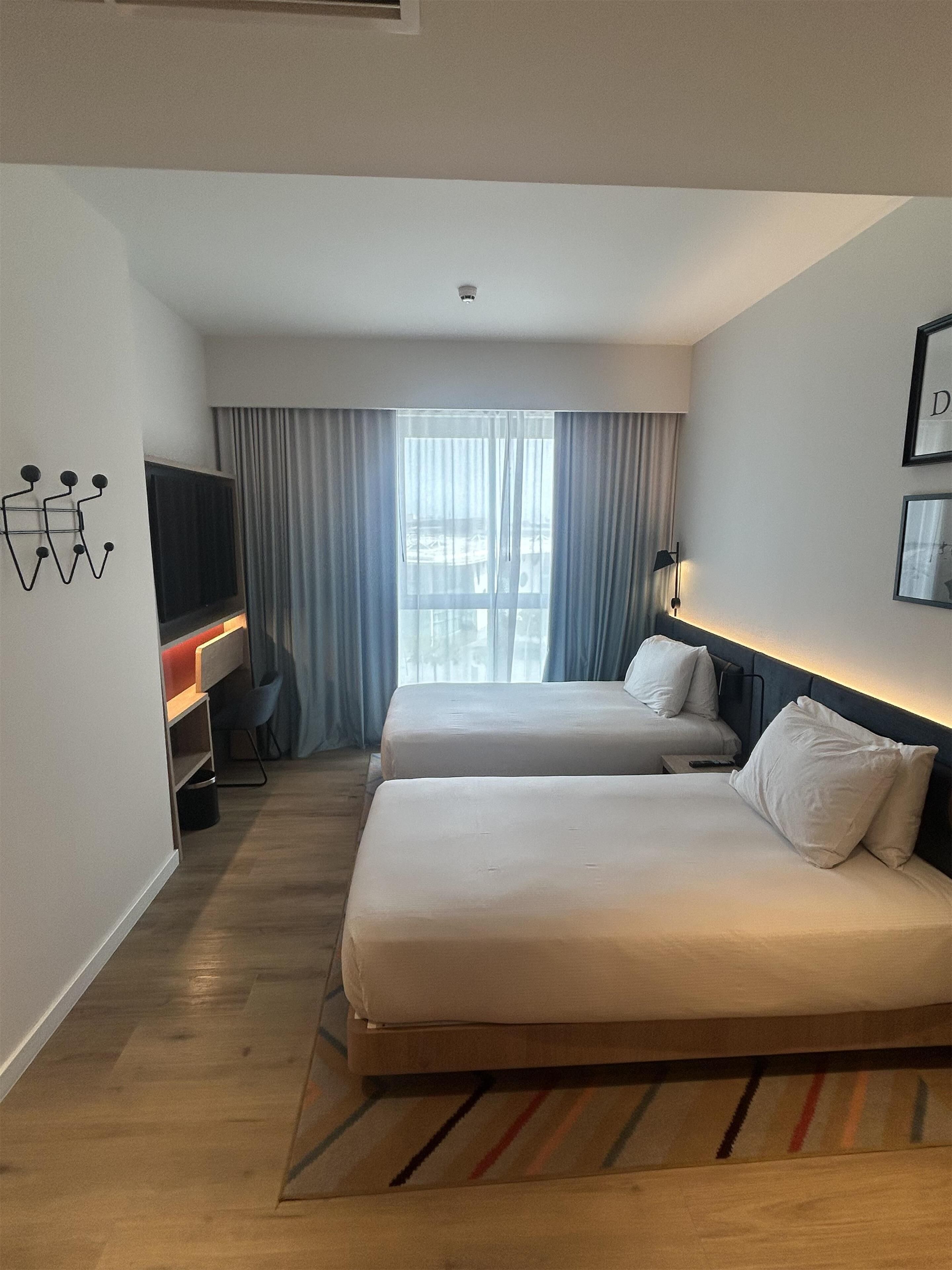 Habitación de hotel con dos camas, televisión, escritorio y ventana con cortinas.
