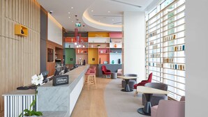 Un moderno vestíbulo de hotel con una recepción, zona de estar y una estantería llena de libros.