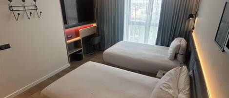 A modern hotel room with two beds, a TV, and a desk.