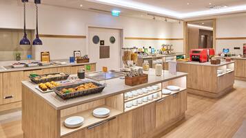 Un área de desayuno moderno en un hotel, con un sistema de buffet que incluye diversas opciones de comida y una máquina de café.