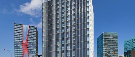 Un immeuble moderne de grande hauteur, doté d’une façade en verre et d’un arc rouge distinctif sur le côté gauche.