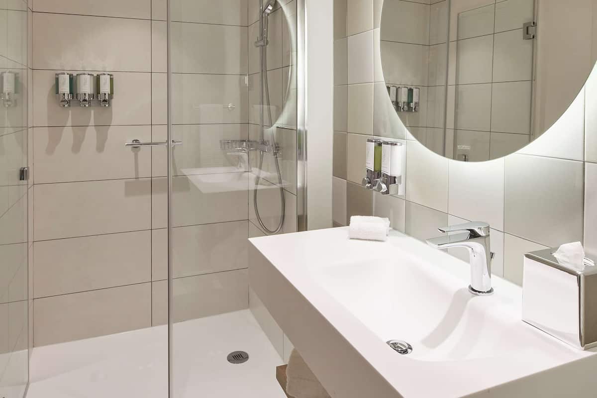 Een moderne badkamer met een douchecabine van glas, een witte wastafel met spiegel en een betegelde vloer.