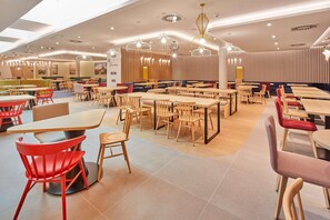 Ein geräumiges Restaurant mit verschiedenen Essbereichen, Holztischen und -stühlen sowie moderner Pendelleuchten.