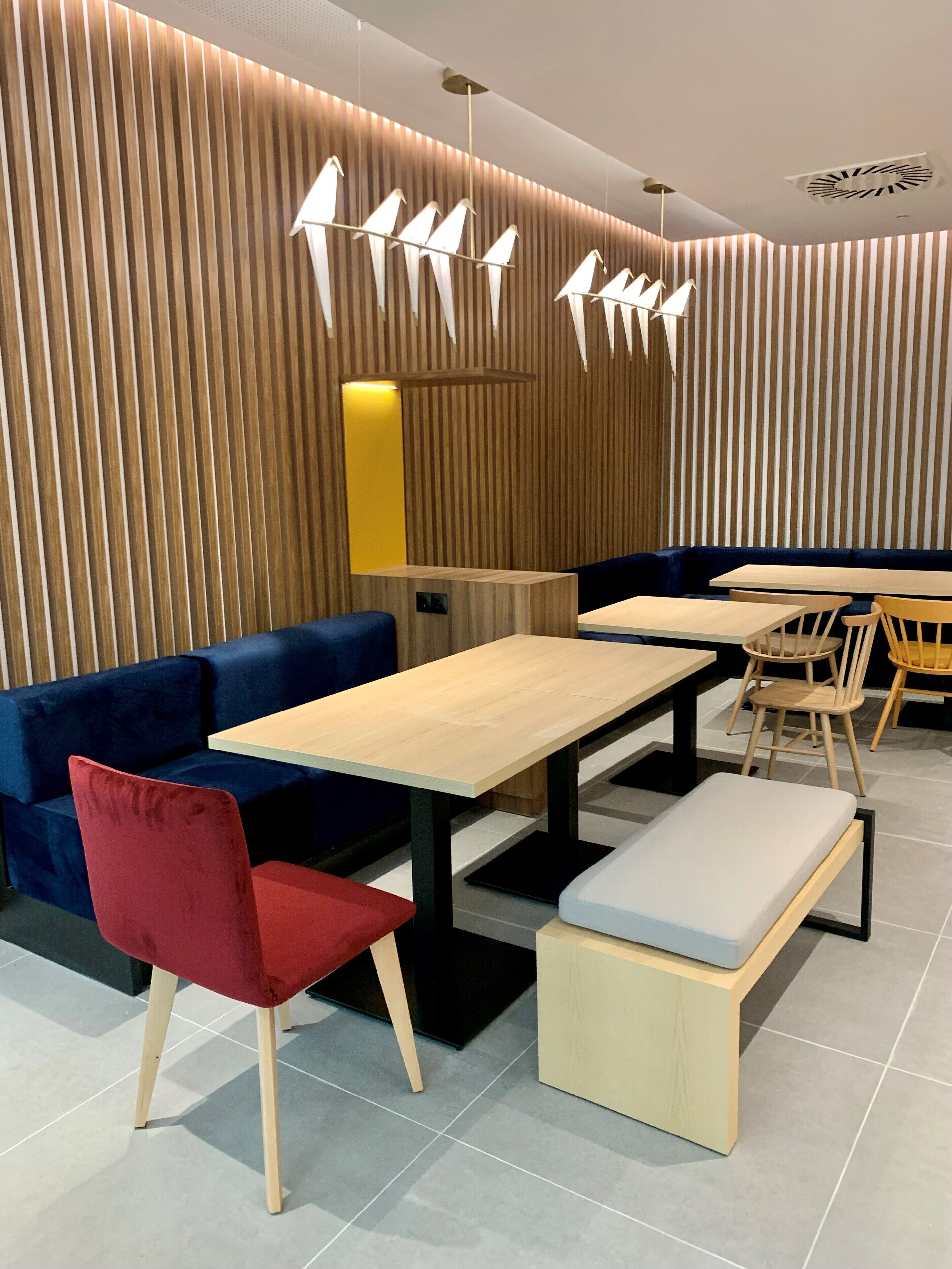A modern interior with a seating area featuring a blue sofa, a red chair, and wooden tables and benches.