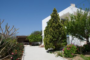 A modern building with a white facade, surrounded by lush greenery and flowering plants. - Family Holidays House Koutsouras by GHH (Ierapetra)