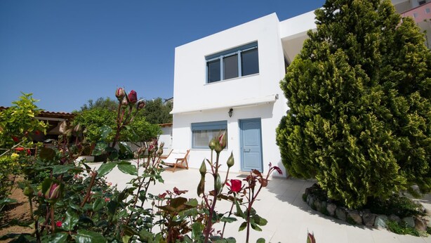 A modern two-story house with a white exterior, a blue door, and a large tree in the front yard. - Family Holidays House Koutsouras by GHH (Ierapetra)