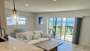 Een moderne keuken met een marmeren aanrecht, een witte bank en een groot raam met uitzicht op een balkon en de oceaan.
