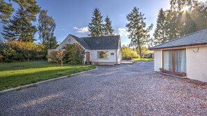 A house with a gravel driveway, a small garden, and a large tree in the background. - Charming 1-bed Cottage in Inverness (Inverness)