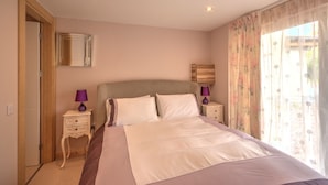 A bedroom with a large bed, two bedside tables with lamps, a mirror, and a window with floral curtains. - Charming 1-bed Cottage in Inverness (Inverness)