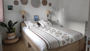 Une chambre à coucher bien rangée, avec un lit en bois, deux lampes de chevet, une plante en pot et des œuvres d’art décoratives accrochées au mur.