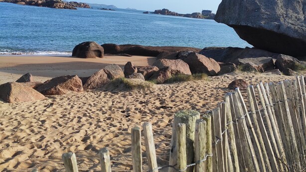 Une plage de sable avec de gros rochers et une clôture en bois.