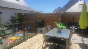 Une terrasse en bois avec une table et des chaises en verre, entourée d’une clôture en bois et d’un toboggan.