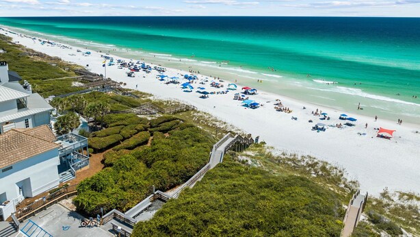 Una playa con un paseo marítimo de madera que lleva a un edificio blanco con techo azul.