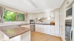 A kitchen with white cabinets, a stainless steel oven, a dishwasher, and a window with curtains.