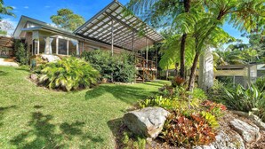 A modern house with a covered patio, a well-maintained lawn, and various tropical plants.