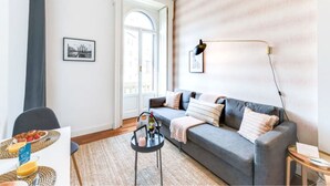 A modern living room with a grey sofa, a small round table with a lamp, and a door leading to a balcony. - Sweett | Arco della Pace (Milano)