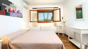 A bedroom with a bed, a window with curtains, a radiator, a desk, and a painting on the wall. - Villa Pantina, 2 bedroom villa near Pollensa (Port de Pollença)