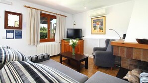 A living room with striped sofas, a television, a fireplace, and a window with curtains. - Villa Pantina, 2 bedroom villa near Pollensa (Port de Pollença)