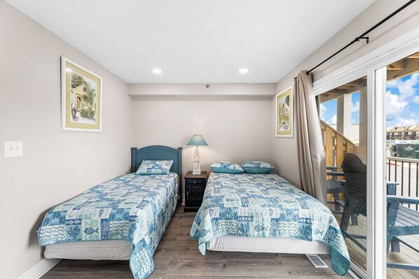 A bedroom with two beds, a nightstand, a lamp, and a view of the outside. - Renovated 3br/2ba townhouse- Groups welcome, Breezy Point 202 (Ocean City)