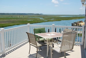 A deck with a table and chairs overlooking a marshy water area.